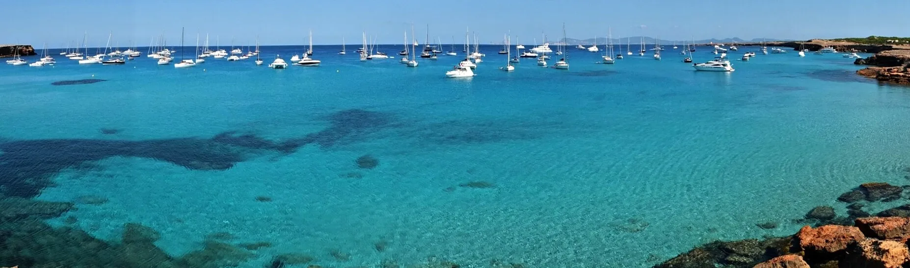 Barcos fondeados en el agua turquesa frente a Cala Saona