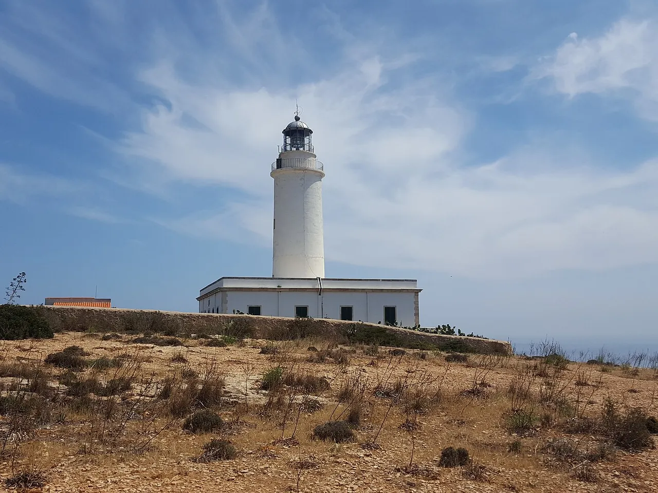 Faro de la Mola blanco sobre el terreno seco de La Mola en Formentera