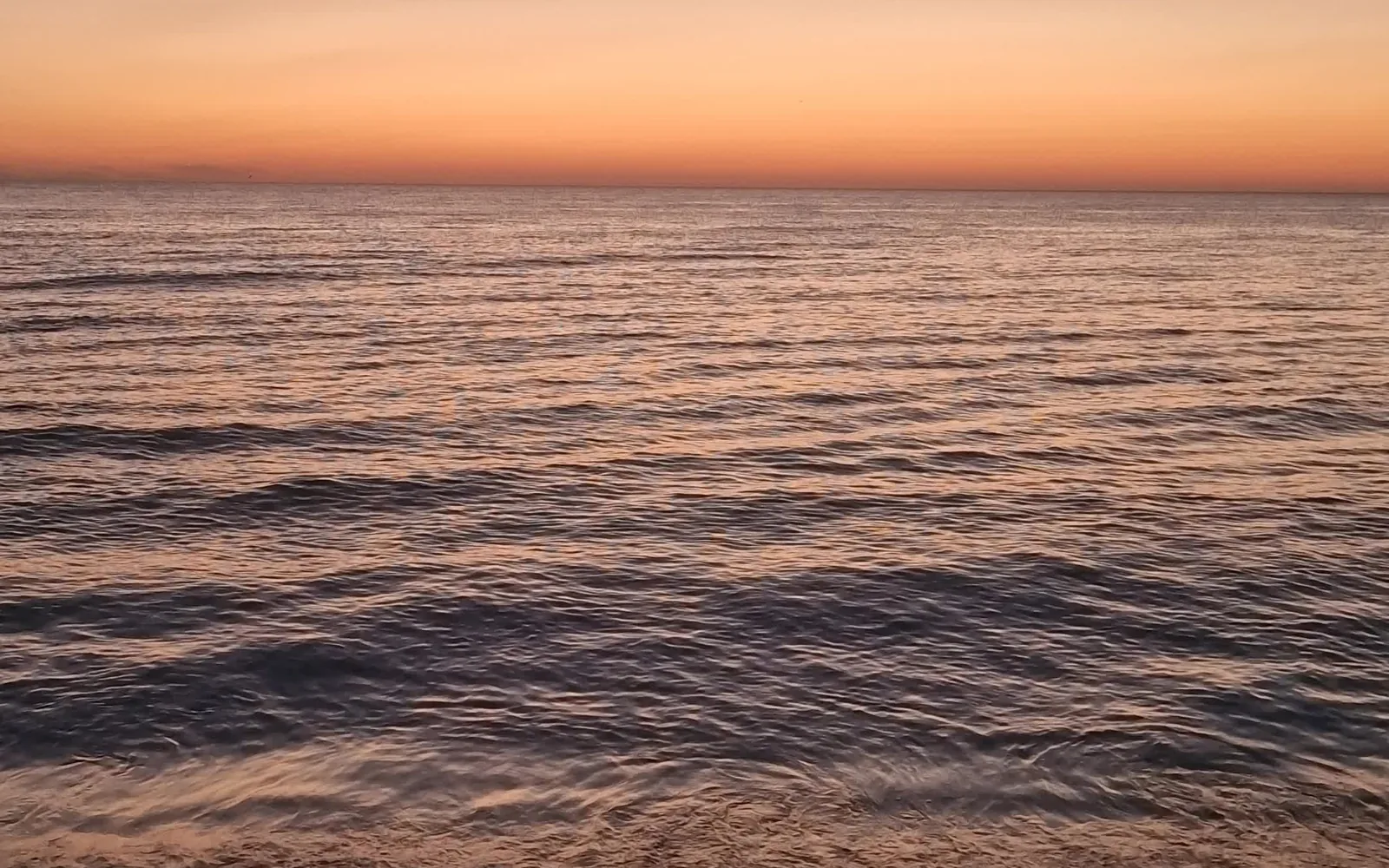 Mar en calma con luz anaranjada en la playa de Daimús