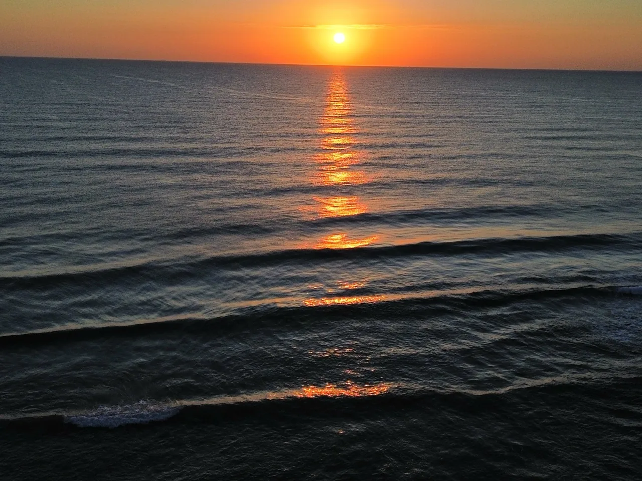 Sol saliendo sobre el mar con reflejo anaranjado en la playa de Daimús